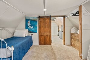 Un dormitorio con una cama, una puerta de madera, un aparador y un cuadro de un velero.