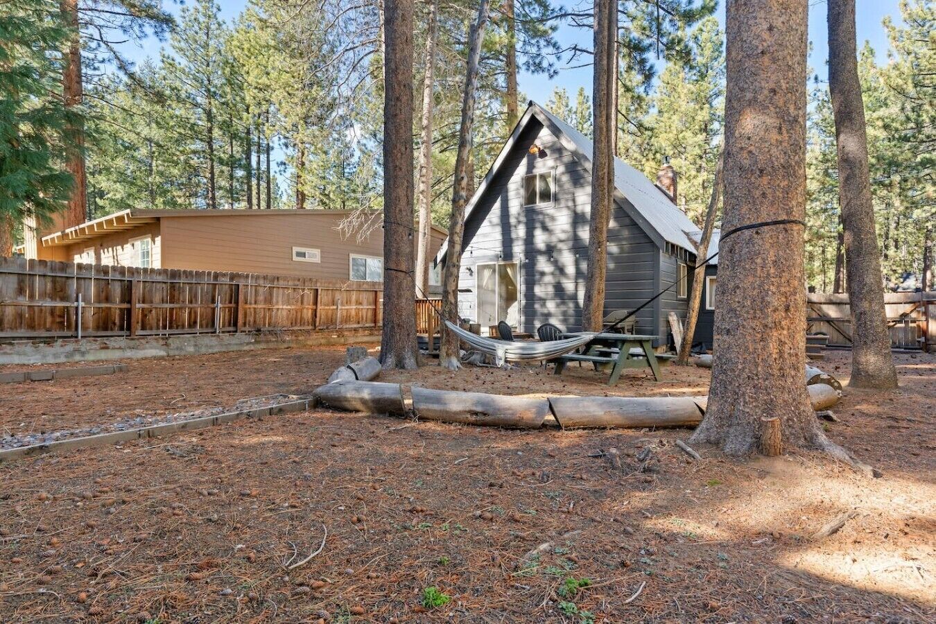 A cabin with a sloped roof, surrounded by trees, and a wooden fence in the background.