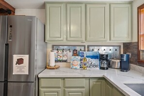 Eine Küche mit grünen Schränken, einem Edelstahl-Kühlschrank, einer Kaffeemaschine und einer Keurig-Kaffeemaschine.