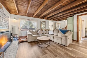Ein gemütliches Wohnzimmer mit Holzbalkendecke, Kamin, Sofa und rundem Couchtisch.