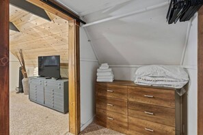 Ein Zimmer mit schrägem Dach, einem Fernseher auf einer Kommode, einem Stapel Handtücher und einer Plastiktüte auf einer Holzkommode.