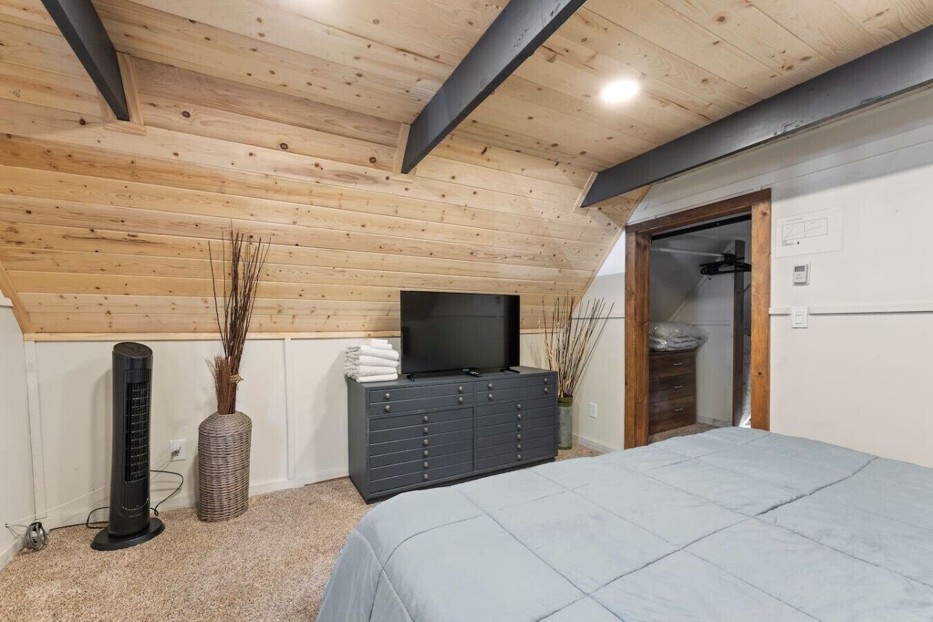 Een slaapkamer met een schuine kap, een bed, een dressoir, een televisie en een radiator.