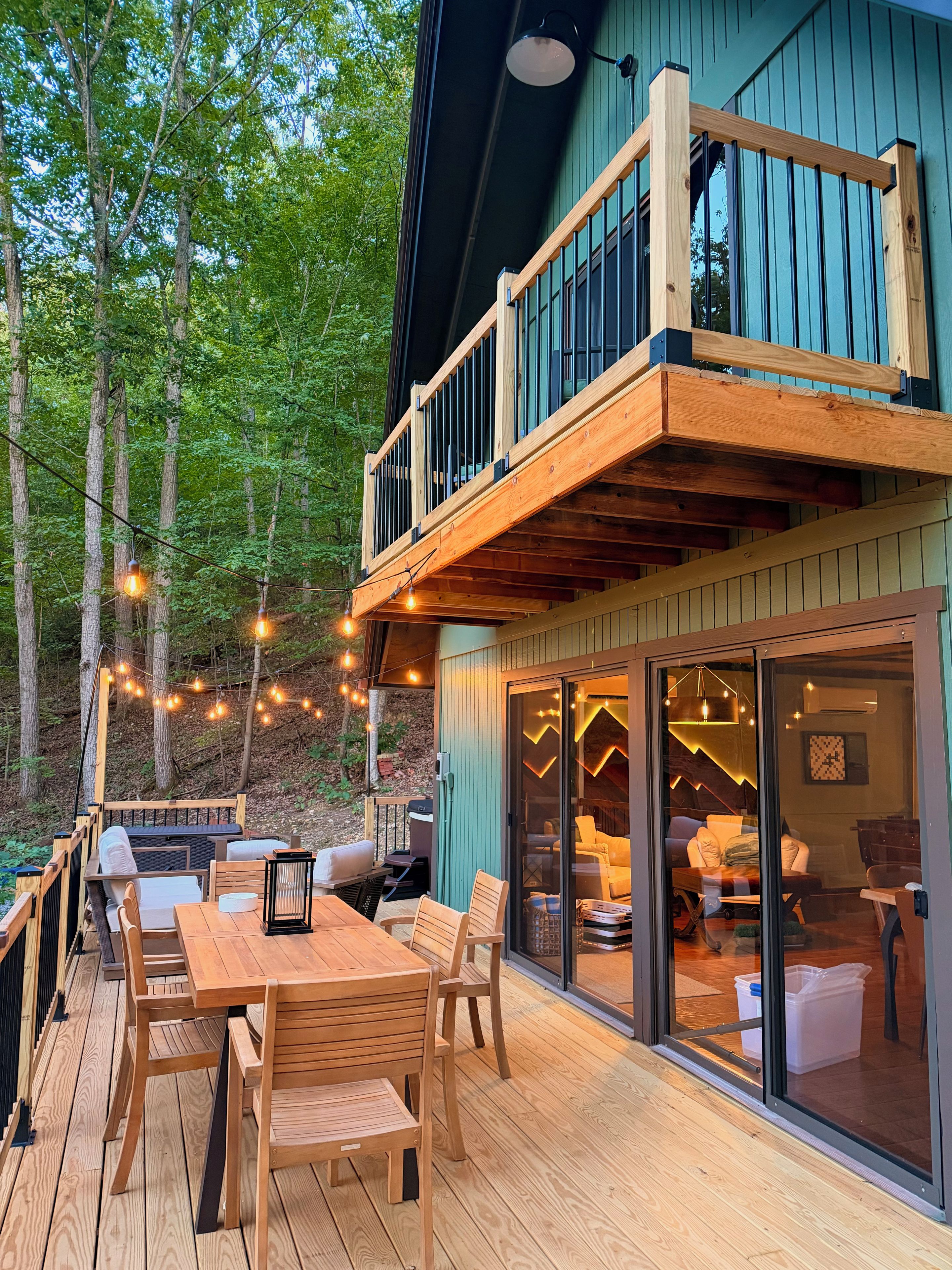 A wooden deck with outdoor furniture, a glass door leading to an interior space, and a balcony with a railing.