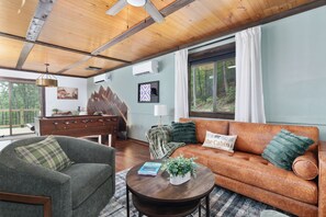 A cozy living room with a wooden ceiling, a sofa, a chair, and a coffee table with a book and a plant. - NEW! Stunning Fall Foliage | Views+ Hot Tub +River Access (Shenandoah)