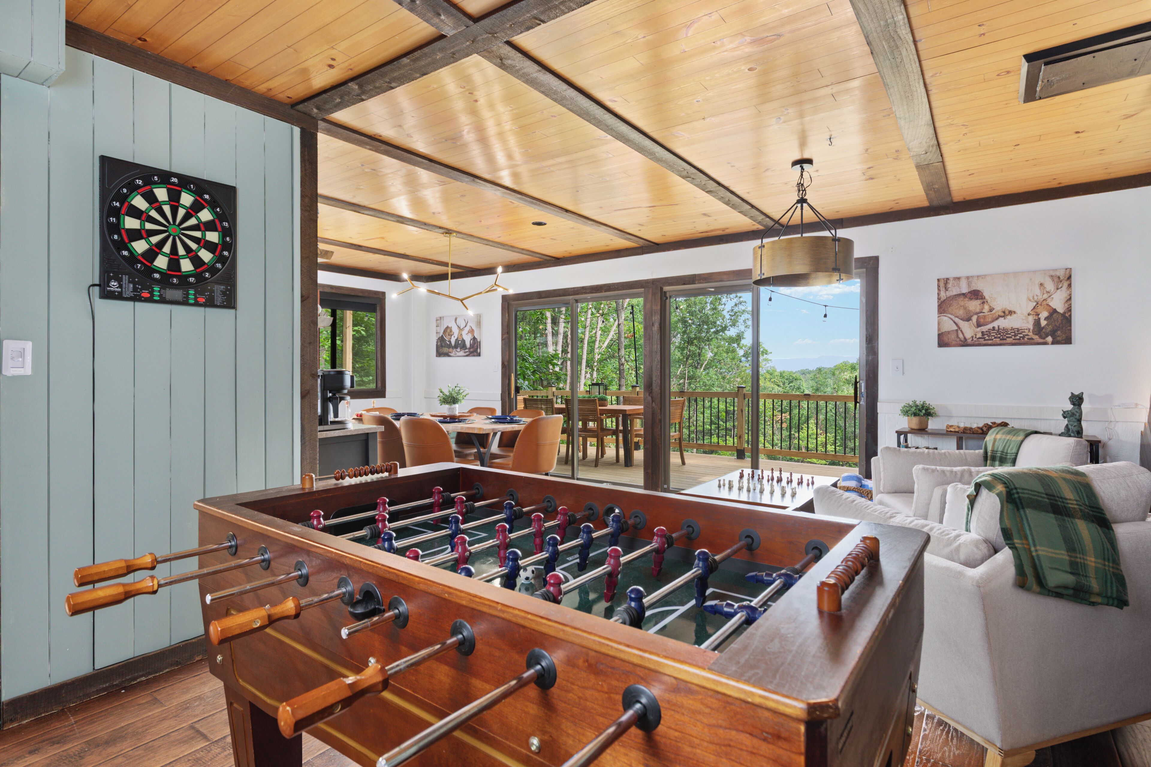 A room with a foosball table, a dartboard, and a dining area with a view of the outdoors.