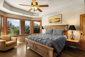Een slaapkamer met een groot bed, een houten hoofdbord, een nachtkastje met een lamp, een stoel en een plafondventilator.