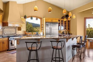 A kitchen with a large island, bar stools, a refrigerator, and hanging pendant lights. - Stunning Tuscany Style Home, Breathtaking 360 Views + Casita! (Cottonwood)