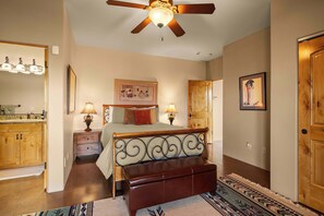 A bedroom with a bed, bedside tables, a ceiling fan, a wooden door, and a bathroom with a sink and mirror. - Stunning Tuscany Style Home, Breathtaking 360 Views + Casita! (Cottonwood)