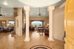 A spacious living area with a stone accent wall, large windows, and a view of the outdoors. - Stunning Tuscany Style Home, Breathtaking 360 Views + Casita! (Cottonwood)