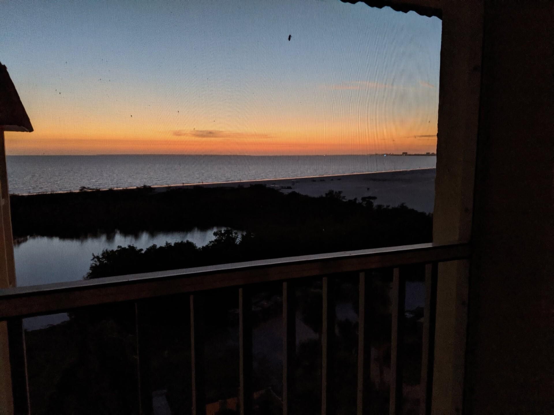 A view of a sunset over a body of water with a bridge in the distance.