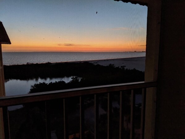 Une vue d’un coucher de soleil sur une étendue d’eau, avec un pont visible au loin.