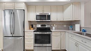 A modern kitchen with stainless steel appliances, white cabinetry, and a tiled backsplash. - Sand Caper #702 (Fort Myers Beach)