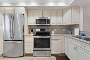 A modern kitchen with stainless steel appliances, white cabinetry, and a tiled backsplash.