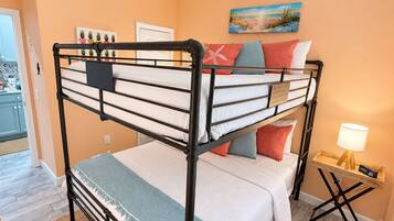 A bunk bed room with a ceiling fan, a painting on the wall, and a bedside table with a lamp.