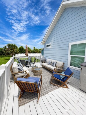 A covered outdoor deck with seating, a table, and a view of the sky.