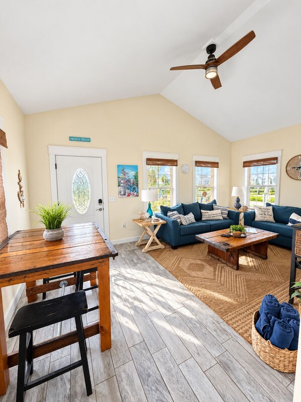 A spacious living room with a wooden table, blue sofa, and a ceiling fan. - Chasing Ray's 2-bedroom, 2-Bath cottage in Mexico Beach, 3 min walk to beach. (Mexico Beach)