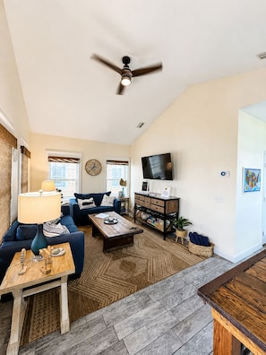 A spacious living room with a ceiling fan, a television, a sofa, a coffee table, and a fireplace.