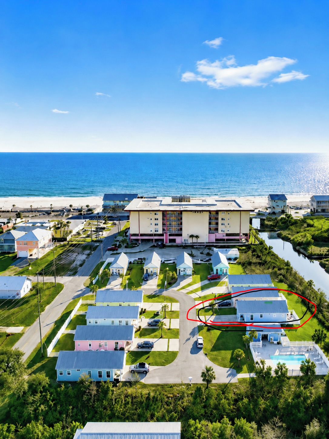 Un quartier résidentiel situé sur la côte, comprenant un grand immeuble, plusieurs maisons et offrant une vue dégagée sur l’océan.