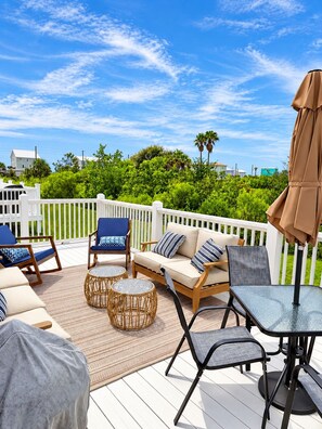 A deck with outdoor furniture, including chairs, a sofa, and a table, surrounded by a white fence and greenery.
