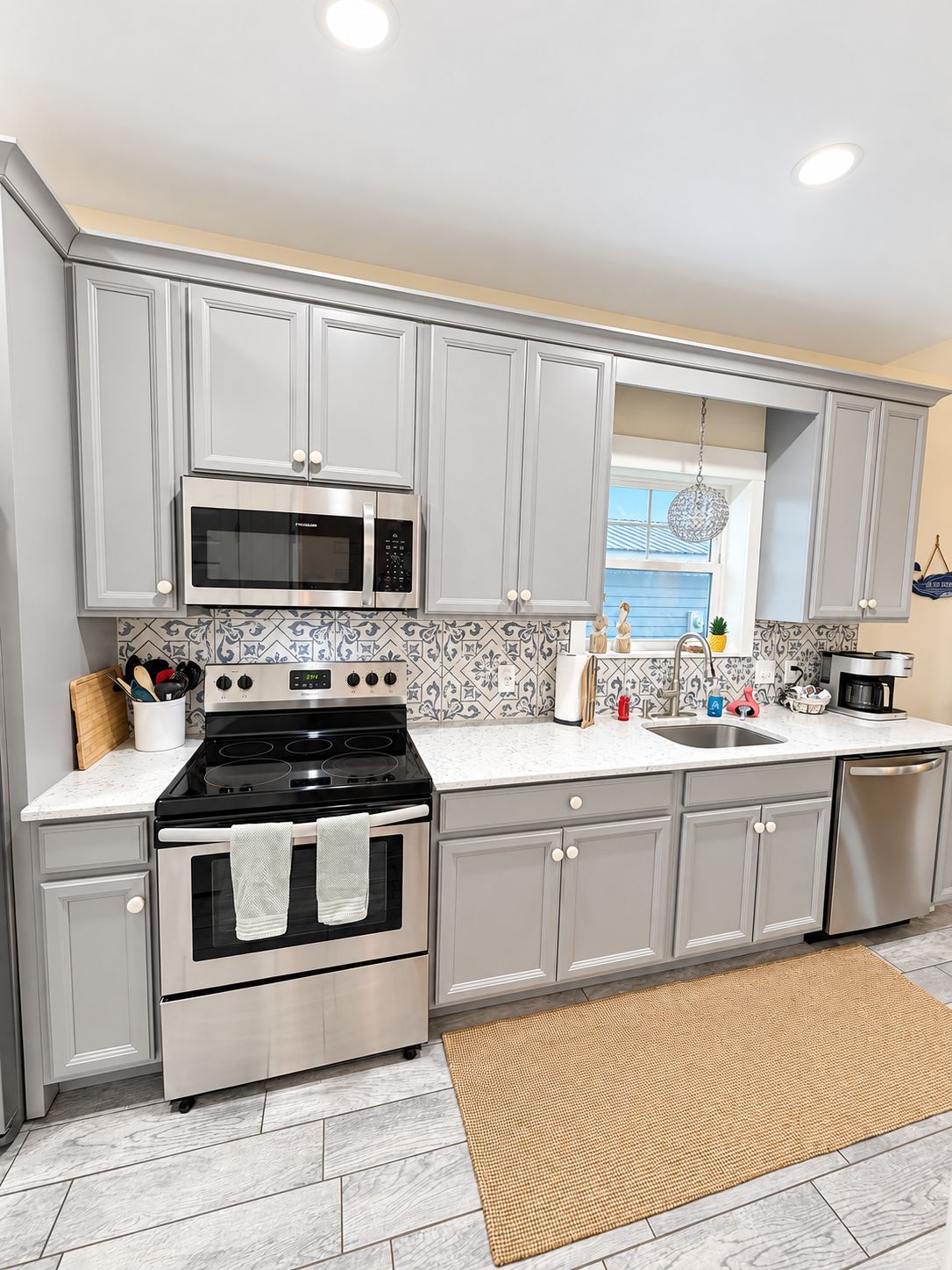 A modern kitchen with grey cabinets, stainless steel appliances, a patterned backsplash, and a view of the outdoors.