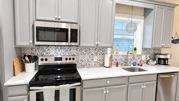 A modern kitchen with grey cabinets, stainless steel appliances, a patterned backsplash, and a view of the outdoors.