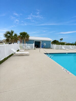 A pool area with lounge chairs and a building with a blue roof.