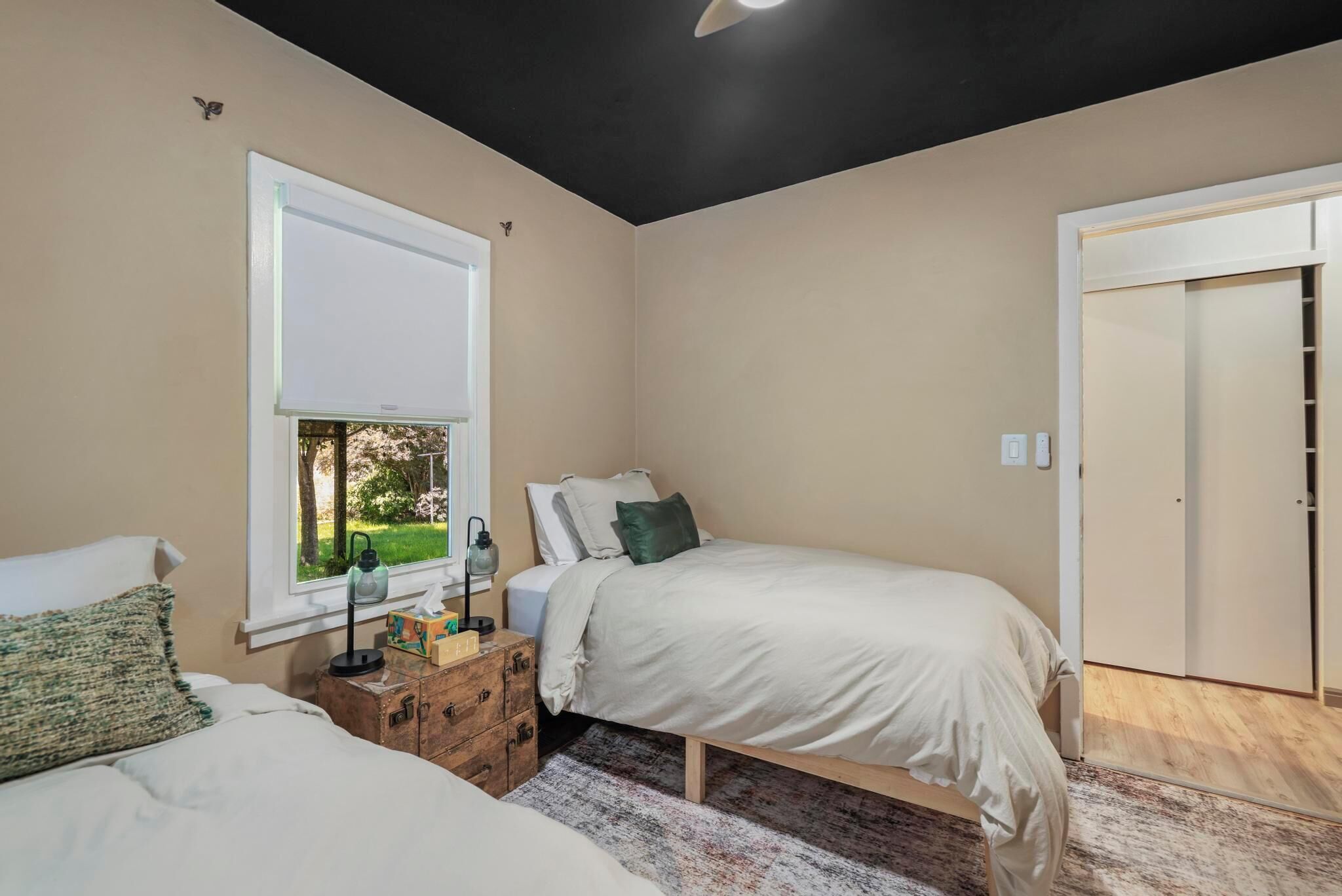 Un dormitorio con cama, ventana, mesita de noche con lámpara y armario.