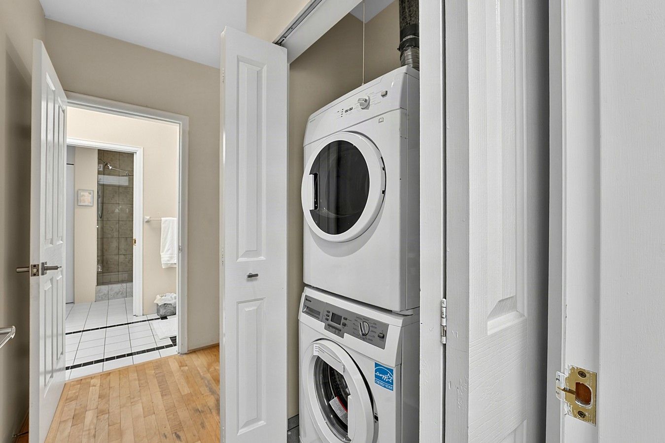 A laundry room with stacked washers and dryers, a door leading to a bathroom, and a tiled floor.