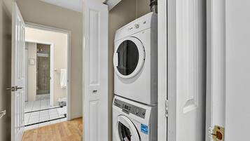 A laundry room with stacked washers and dryers, a door leading to a bathroom, and a tiled floor.