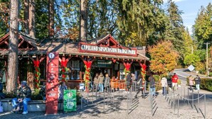 Un edificio de madera rústico con un letrero que dice 'Capilano Suspension Bridge Park', una taquilla y un área de entrada cercada.