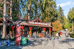 A rustic wooden building labeled 'Capilano Suspension Bridge Park' with a ticket booth and a fenced entrance area.