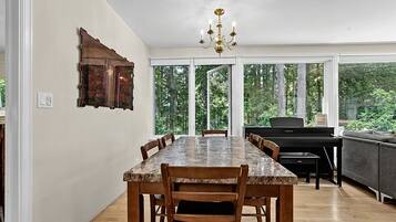 Un espace repas comprenant une table en marbre, des chaises en bois, un piano et une vue sur la forêt grâce à de grandes fenêtres.