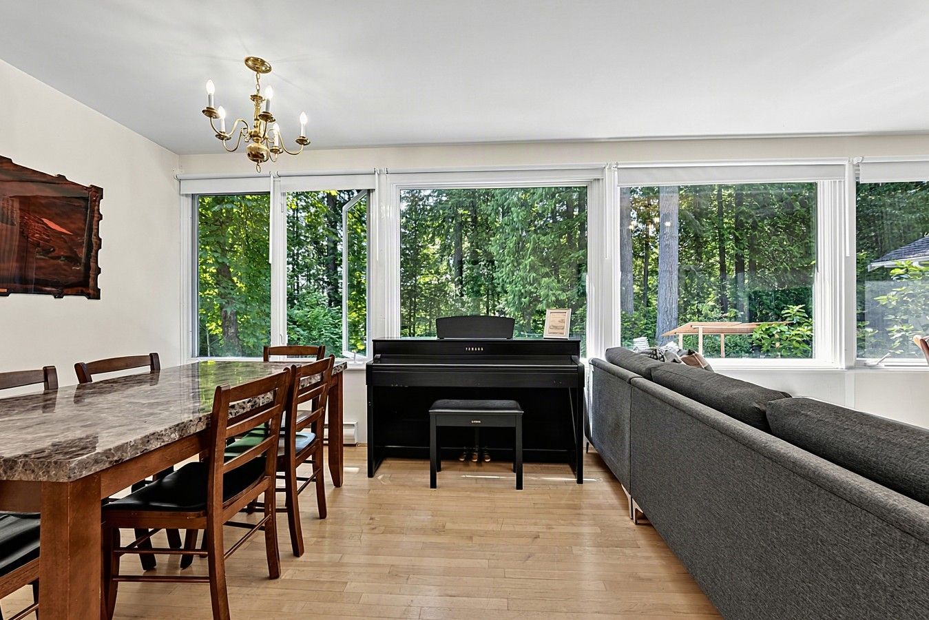 A dining area with a marble table, wooden chairs, a piano, and a grey sofa.