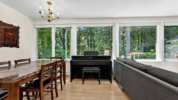 A dining area with a marble table, wooden chairs, a piano, and a grey sofa.