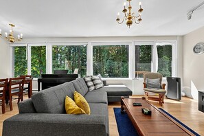 Un salon moderne comprenant un canapé d’angle, un piano, un téléviseur et un coin repas avec des chaises.