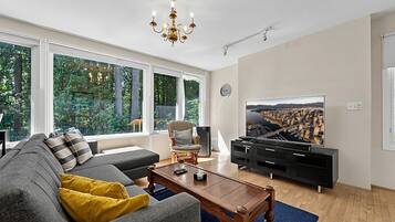 A modern living room with a sofa, coffee table, TV, and a large window with a cityscape view.