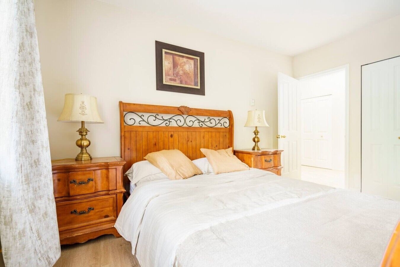 A bedroom with a wooden bed, two bedside tables with lamps, a framed picture on the wall, and a white door.