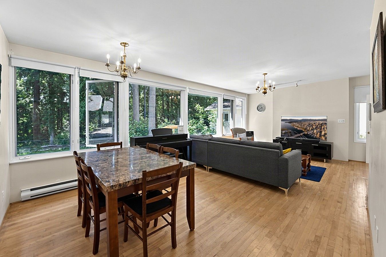 A spacious living room with a dining area, large windows, and a piano.