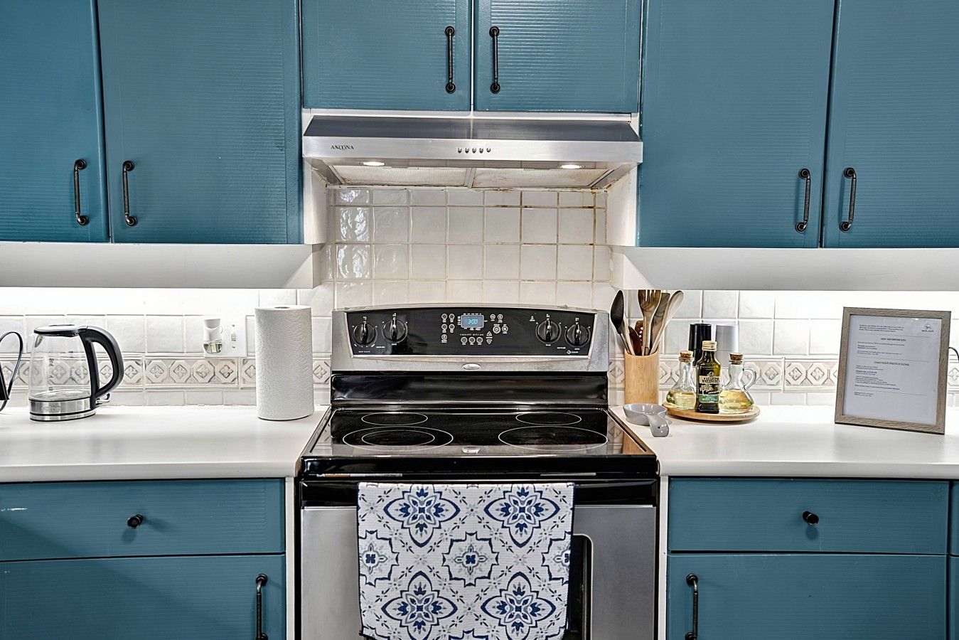 Une cuisine avec des armoires de couleur turquoise, une cuisinière en acier inoxydable et un dosseret carrelé.