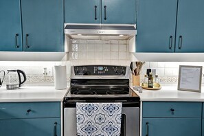 A kitchen with teal cabinets, a stainless steel stove, and a tiled backsplash.