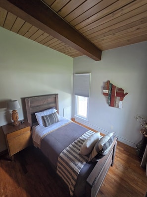 A bedroom with a wooden ceiling, a bed with a headboard, a nightstand, a window with blinds, and a wall decoration. - Mid-Century Modern Retreat Near Sand Valley and Lakes (Wisconsin Rapids)