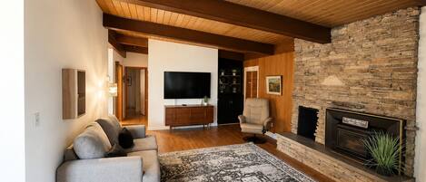 Una sala de estar con chimenea de piedra, un sofá, un televisor y un tapete estampado.