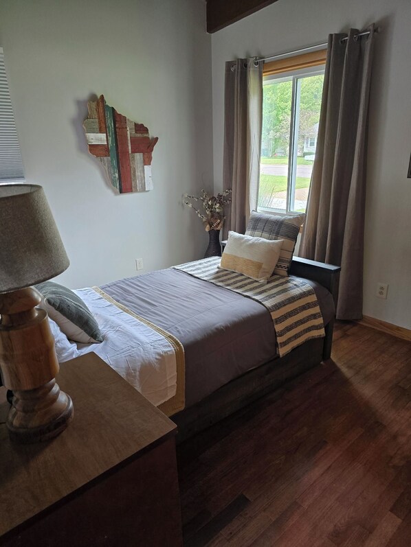 A bedroom with a bed, a lamp, a window with curtains, and a wall decoration.