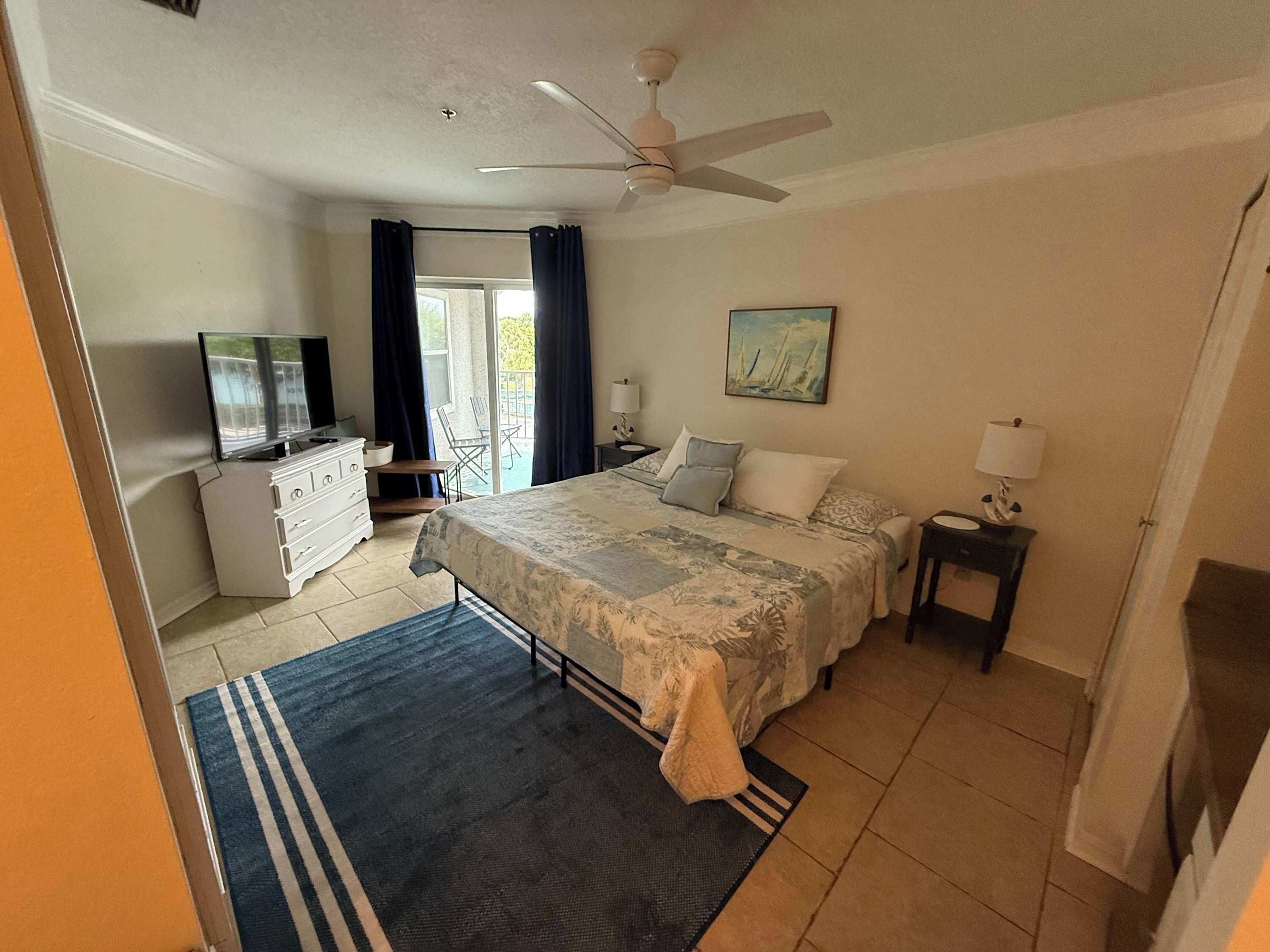 A bedroom with a bed, a TV, a desk, a chair, and a painting on the wall.