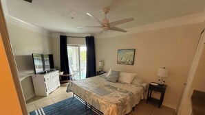 A bedroom with a bed, a TV, a desk, a chair, and a painting on the wall. - Ocean Gate I: Cozy Retreat Near Beach (St. Augustine)