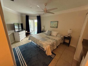 A bedroom with a bed, a TV, a desk, a chair, and a painting on the wall. - Ocean Gate I: Cozy Retreat Near Beach (St. Augustine)