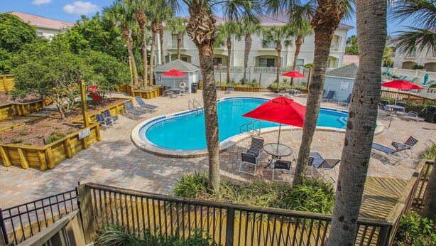 A swimming pool surrounded by palm trees and lounge chairs, with a building in the background. - Ocean Gate I: Cozy Retreat Near Beach (St. Augustine)