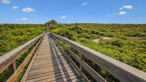 A wooden boardwalk leading to a small structure in a lush, green landscape. - Ocean Gate I: Cozy Retreat Near Beach (St. Augustine)