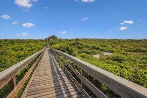 A wooden boardwalk leading to a small structure in a lush, green landscape. - Ocean Gate I: Cozy Retreat Near Beach (St. Augustine)