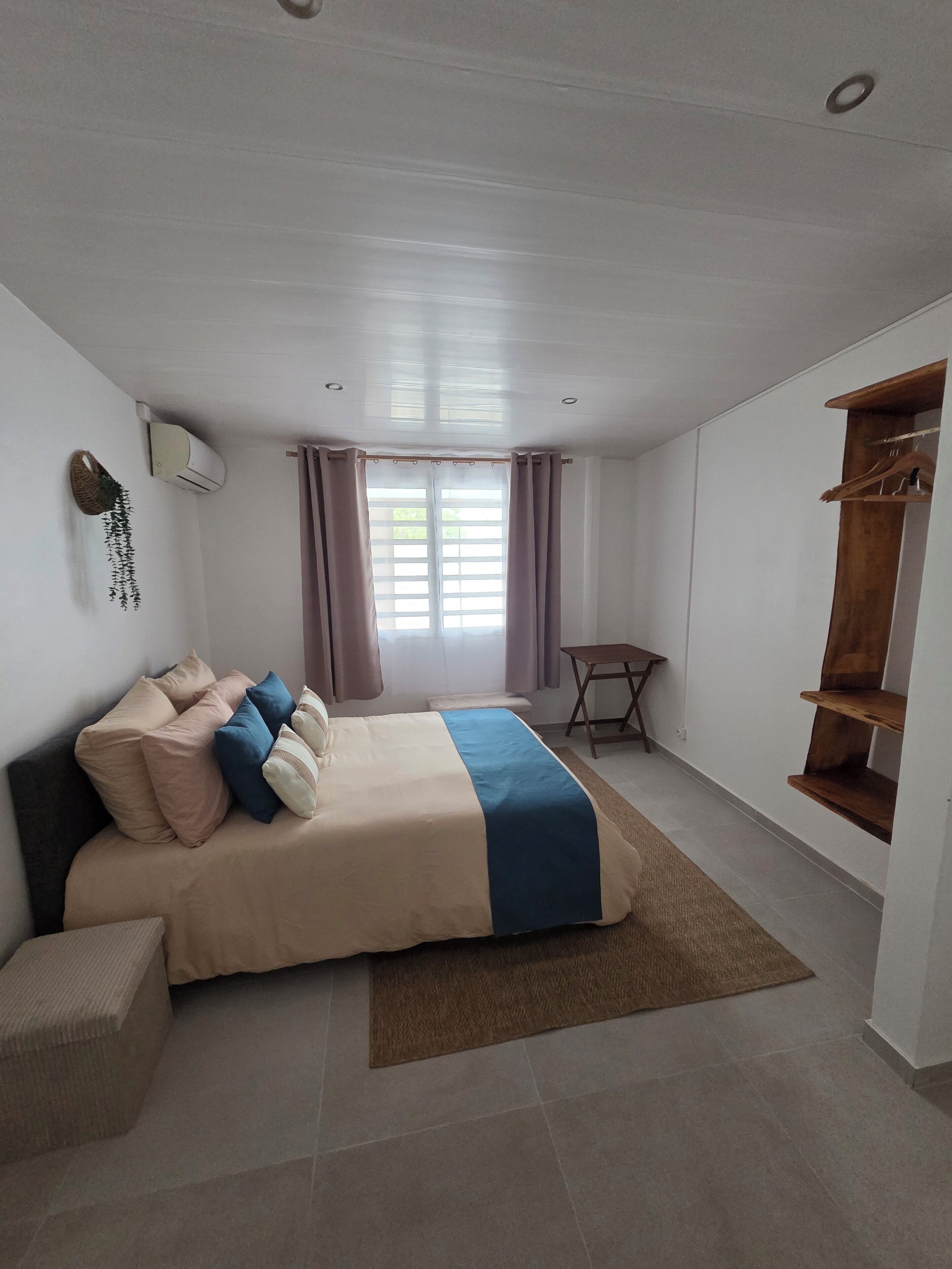 A bedroom with a bed, a small table, a shelf, and a window with curtains.
